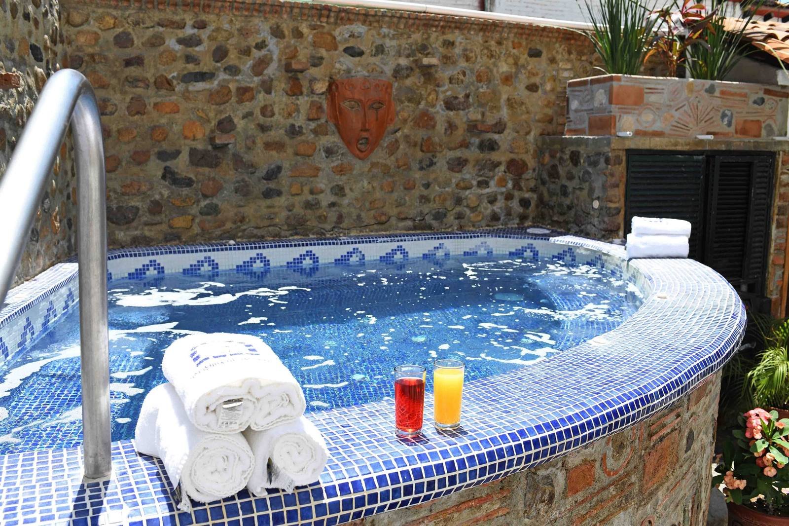 Petit Hotel Pilitas: the stone hot tub with blue tiles, rolled towels and two drinks on the edge